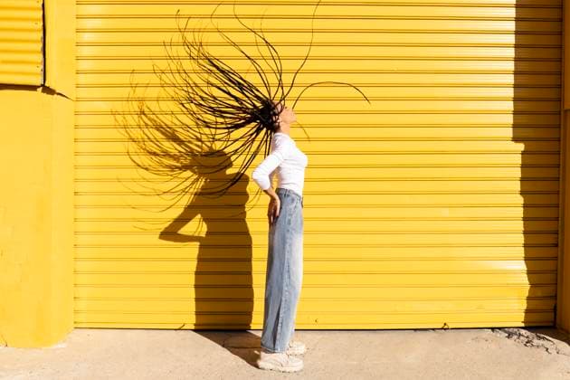 Creative Highlights Symbolbilder Woman tossing hair in front of yellow corrugated shutter model released, Symbolfoto, LMCF00777