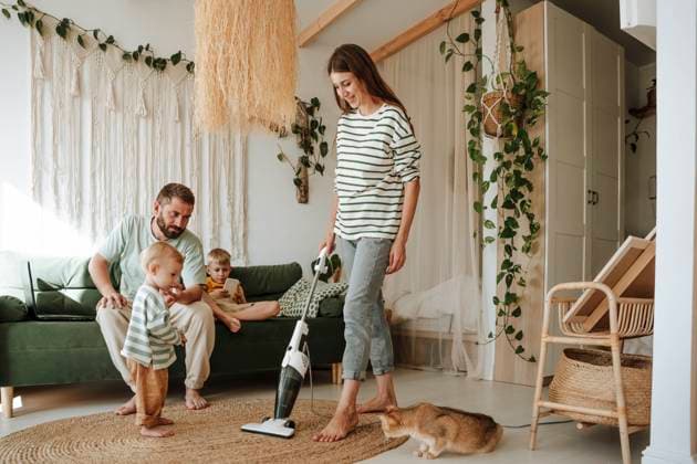 IMAGO Creative: Frühjahrsputz Mother vacuuming the living room at home with family watching model released, Symbolfoto property released, WESTF25280