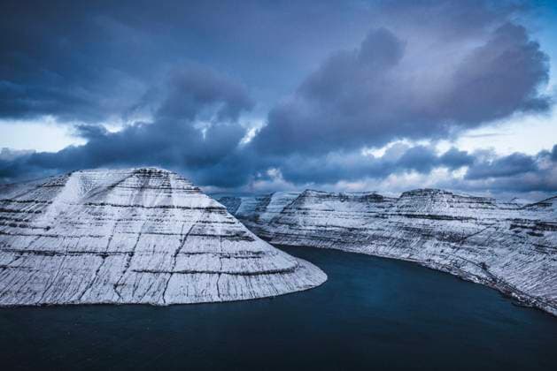 View of snow covered mountains and clouds towering over a fjord Klaksvík, Northern Isles, Faroe Islands CR_SSNF240118-1314151-01