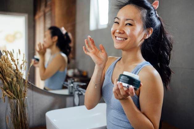Smiling Asian young woman applies moisturizing cream or sunscreen to her face while standing in front of mirror in bathroom at home. Lovely Korean girl takes care of her skin. Smiling Asian young woman applies moisturizing cream or sunscreen to her face while standing in front of mirror in bathroom at home. Lovely Korean girl takes care of her skin. Cosmetics and beauty. ,model released, Symbolfoto Copyright: xZoonar.com DashaxPetrenkox 20906551 ,model released, Symbolfoto ,property released