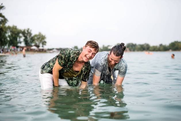Wet young men friends at summer festival, standing in lake. Wet young men friends at summer festival, standing in lake and looking at camera. model released Copyright: xx Uprising_2019_1831
