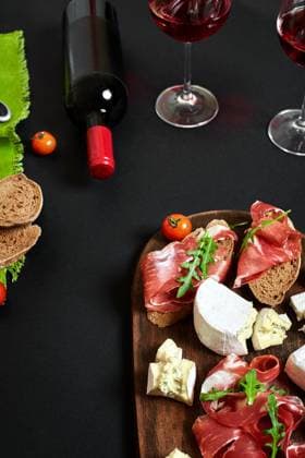 Prosciutto, salami, baguette slices, tomatoes and nutson rustic wooden board, two glasses of red wine over black background Cheese and meat appetizer selection. Prosciutto, salami, baguette slices, tomatoes and nutson rustic wooden board, two glasses of red wine over black background. Still life Copyright: xZoonar.com Derich_Anreyx 20951248