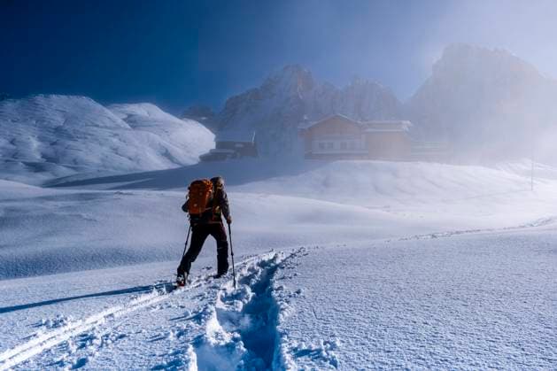 A ski tourer walking to the mountain hut Baita Segantini through fog, the summits of the Pale group in the distance, in winter. San Martino di Castrozza Trentino-Alto Adige Italy FB_2023_3710