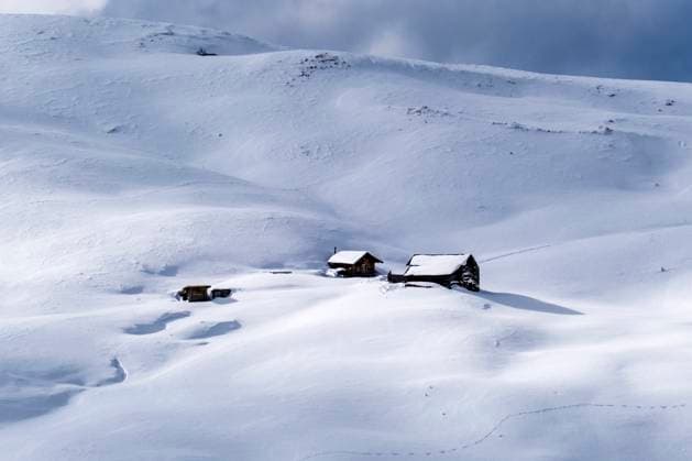 Some snow-covered wooden houses on the slopes of Passo Sella pass in winter. Canazei Trentino-Alto Adige Italy FB_2023_3865