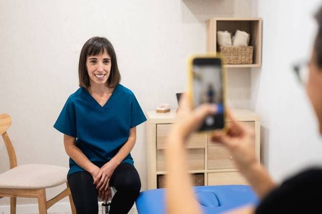 A cheerful female healthcare worker in scrubs poses for a photo, with her image captured on a smartphone by another person Model Released HodeiUnzueta_ID18737_558188_002 Copyright: xHodeixUnzuetax RECORD DATE NOT STATED