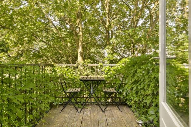 This tranquil balcony features a black metal table and chairs amidst flourishing trees and plants, providing a serene urban escape. Model Released ProCreators_ID17593_532594_009 Copyright: xProxCreatorsx RECORD DATE NOT STATED