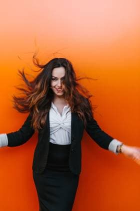 Creative Highlights Symbolbilder A smiling woman looking at camera in professional attire flicks her hair against a vibrant orange wall, capturing a moment of carefree happiness in Madrid, Spain. Model Released VictorTorres_ID19611_581799_049 Copyright: xVictorxTorresx