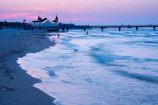  Ruhige Abendstimmung am Strand mit ruhigen Wellen und zwei Person nahe einer Seebrücke mit Gebäude in der Abenddämmerung, klarer, blau-violetter Himmel mit rosa Wolken, Seebrücke Ahlbeck im letzten Abendlicht, Bewegungsunschärfe, Wischeffekt, Langzeitbelichtung, Blick vom westlichen Strand, Seebad Ahlbeck, Insel Usedom, Mecklenburg-Vorpommern, Deutschland, Europa *** quiet Abendstimmung on Beach with quiet Waves and Two Person near a Seabridge with Building in the Dusk, clearer, Blue purple Sky with Pink Clouds, Seabridge Ahlbeck at last Evening light, Motion blur, Wiping effect, Long exposure, View from Western Beach, Seaside resort Ahlbeck, Island Usedom, Mecklenburg Western Pomerania, Germany, Europe Copyright: imageBROKER/CarolaxVahldiek ibxcva10113590.jpg