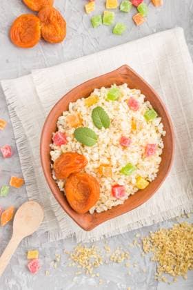 Bulgur Brei mit getrockneten Aprikosen und kandierten Früchten in einer Tonschüssel auf grauem Betonhintergrund und Leinentextil. Ansicht von oben, flach gelegt, Nahaufnahme. Türkische traditionelle Küche *** Bulgur Porridge with dried Apricots and candied Fruit in a Tonschüssel at grey Concrete background and Linen textile View from above, flat placed, Close-up Turkish traditional Kitchen Copyright: imageBROKER ULADZIMIRxZGURSKI ibxuzg10136688.jpg