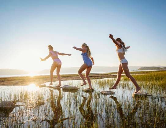 Girls (10-11, 12-13, 14-15) walking on stepping stones in lake at sunrise , 20.12.2023, model released, TTBB_ti0007_02286.jpg, Pre-Adolescent Child,Girls,10-11 Years,12-13 Years,Teenager,Teenage Girls,14-15 Years,Outdoors,Sunrise,Horizontal,Arms Raised,Walking,Sister,Family,Sun,Sunlight,Clear Sky,Summer,Landscape,Scenics,Tranquility,Lake,Lakeshore,Vacations,Rock,Vitality,Reeds,Ba Copyright: xErikxIsaksonx