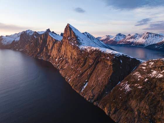 Creative Highlights World Drone shot of snow covered cliff by sea against sky at sunset Senjahopen, Troms og Finnmark fylke, Norway CR_BRHU240206-1329098-01