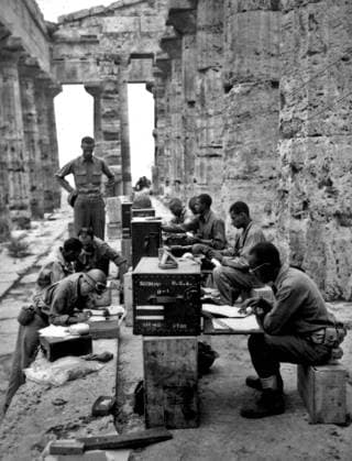 A makeshift office set up between the columns of the Greek temple of Neptune, Italy, 22nd September, 1943 (b w photo) 1721279 A makeshift office set up between the columns of the Greek temple of Neptune, Italy, 22nd September, 1943 (b w photo) by Unknown photographer, (20th century); (add.info.: Italy. September 22, 1943 : A company of men has set up its office between the columns (Doric) of an ancient Greek temple of Neptune. At desk, front to rear: Sgts. James Shellman, Gilbert A. Terry, John W. Phoenix, Curtis A. Richardson, and Leslie B. Wood. In front of desk, front to rear: T Sgt. Gordon A. Scott, M Sgt. Walter C. Jackson, Sgt. David D. Jones, and WO Carlyle M. Tucker. Italy. September 22, 1943). Copyright: xBridgemanxImagesx 1721279