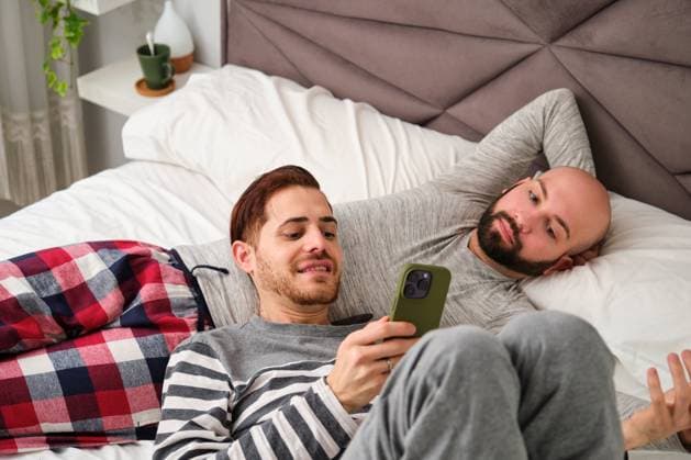 Homosexual couple using the phone together relaxing in bed. Madrid, Community of Madrid, Spain CR_CRVI240207D-1347121-01 ,model released, Symbolfoto