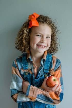 Little girl with curly hair wears overalls holding an apple Valdosta, Georgia, United States CR_HZPG240205-1347229-01 ,model released, Symbolfoto