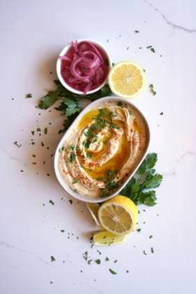 Chickpea hummus served with olive oil, pickled red onion, lemons, and flatbread on a white marble table background. Minimal layout flatlay. Chickpea hummus served with olive oil, pickled red onion, lemons, and flatbread on a white marble table background. Minimal layout flatlay. Copyright: xMilleflorexImagesx MIL150124-22