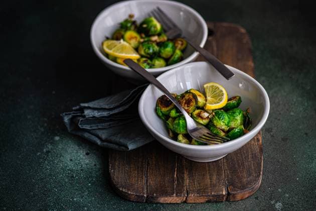 From above of bowl of grilled Brussels sprouts seasoned with garlic and spices, garnished with a slice of lemon, served on a wooden board with a fork Model Released AnnaBogush_ID19160_569959_003 Copyright: xAnnaxBogushx