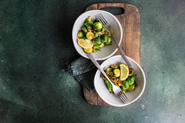 Top view of bowl of grilled Brussels sprouts seasoned with garlic and spices, garnished with a slice of lemon, served on a wooden board with a fork Model Released AnnaBogush_ID19160_569961_004 Copyright: xAnnaxBogushx