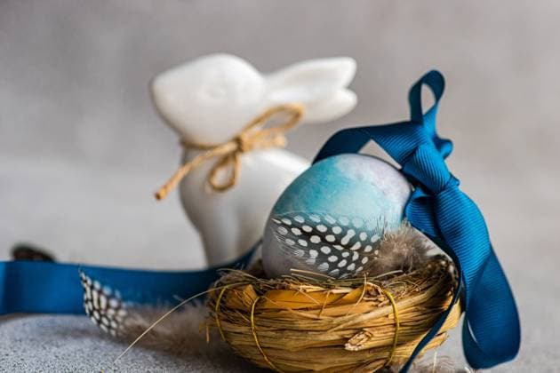 A close up Easter composition with a blue dyed egg adorned with a ribbon in a nest, guinea fowl feather, and a ceramic rabbit on a textured background Model Released AnnaBogush_ID19161_569979_006 Copyright: xAnnaxBogushx