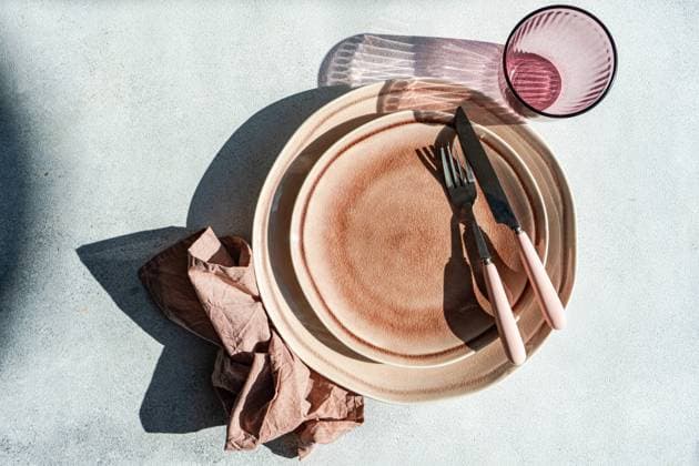 From above sophisticated Easter table setting featuring stacked ceramic plates, rose gold cutlery, and a linen napkin on a textured background. Model Released AnnaBogush_ID19406_575242_008 Copyright: xAnnaxBogushx