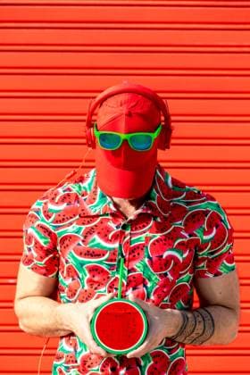 Anonymous man in printed shirt covering face with hat Unrecognizable street style male with hat covering face and wearing sunglasses headphones in place while standing in printed water melon slices shirt and carrying mock juice against red background Model Released SergioVictorVega_ID19622_581839_004 Copyright: xSergioxVictorxVegax RECORD DATE NOT STATED