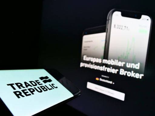Smartphone with company logo of German online broker Trade Republic Bank GmbH on screen in front of webpage. Focus on phone center-left of display. 3034884