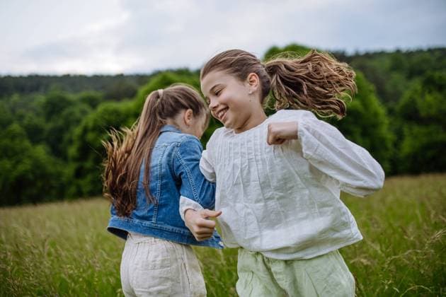 Two sisters playing at meadow in grass, having fun, running and dancing. Sisterly love and siblings relationship concept. Two sisters playing at meadow in tall grass, running and dancing, having fun. Sisterly love and siblings relationship concept. model released