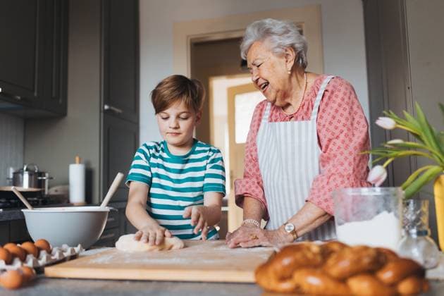 Grandmother with grandson preparing traditional easter meals, kneading dough for easter cross buns. Passing down family recipes, custom and stories. Grandmother with grandson preparing traditional easter meals, kneading dough for easter cross buns. Passing down family recipes, custom and stories. Concept of family easter holidays. model released