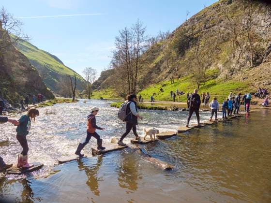 People crossing Stepping Stones over the River Dove in the Peak District, England, UK People crossing Stepping Stones over the River Dove in the Peak District, England, UK. Copyright: 4060_19_AFS-2023-00276