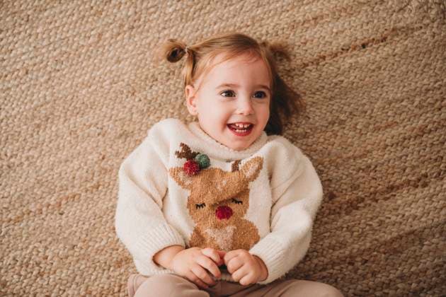 Smiling girl wearing Christmas sweater and lying on carpet at home model released, Symbolfoto property released, EBBF08339