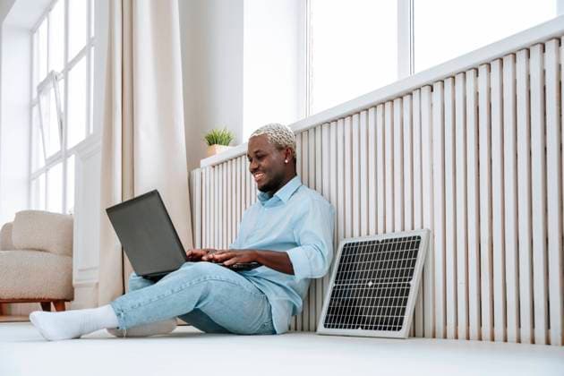 Creative Highlights Symbolbilder Smiling freelancer sitting near solar panel and using laptop at home model released, Symbolfoto property released, NLAF00318