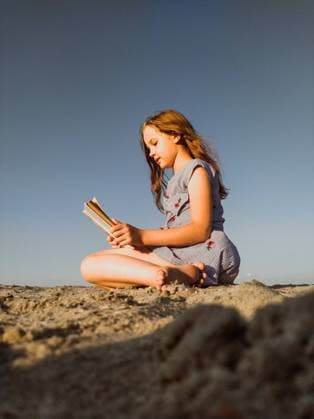 Creative Highlights Symbolbilder Little girl reading a book sitting on the sand against the sky Zatoka, Odessa Oblast, Ukraine R_SVLA220114-898771-01 ,model released, Symbolfoto
