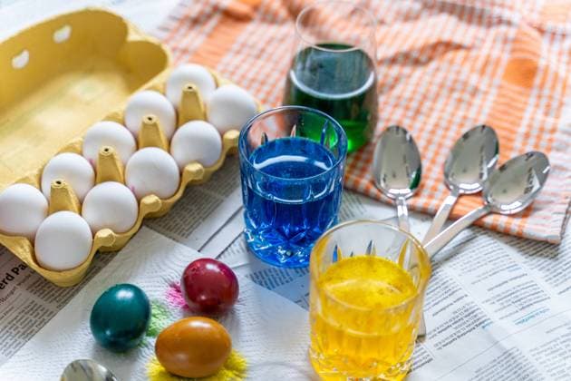 Augsburg, Bavaria, Germany - 28 February 2024: Easter egg dyeing concept, table covered with newspaper, egg dyes in jars and colorful eggs for Easter *** Ostereier Färben Konzept, Tisch mit Zeitung ausgelegt darauf Eierfarben in Gläsern und bunte Eier zu Ostern