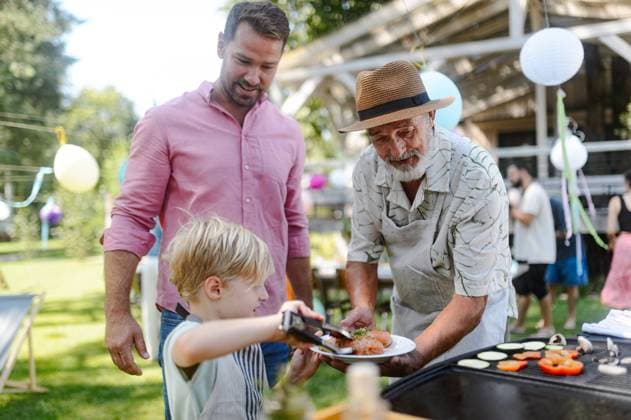 Father, grandfather and son grilling together at garden BBQ. Three generations of men at summer family garden party. Father, grandfather and son grilling together at a garden bbq party. Three generations of men at summer family garden party. model released
