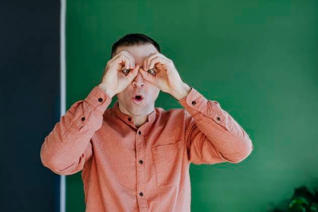 Creative Highlights Symbolbilder Surprised man staring through finger binoculars in front of green wall model released, Symbolfoto property released, YTF01665