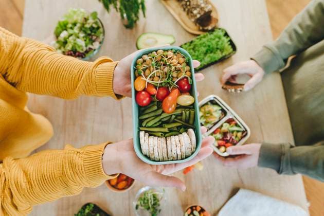 IMAGO Creative, Food, Trend, Meal Prep Hands of woman holding vegetarian food lunch box near man at table model released, Symbolfoto property released, YTF01686