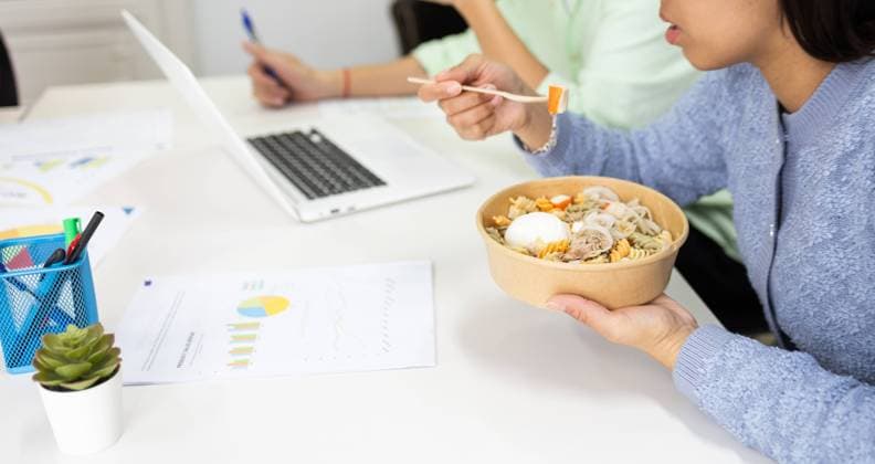 A person enjoys a healthy bowl of noodles with vegetables and egg during a busy workday, promoting productivity and well-being. Model Released DavidMunoz_ID19491_576509_063 Copyright: xDavidxMunozx