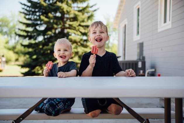 Two boys sitting on picnic table making silly faces with popsicles. Bismarck, North Dakota, United States CR_KIFR240228-1358312-01 ,model released, Symbolfoto