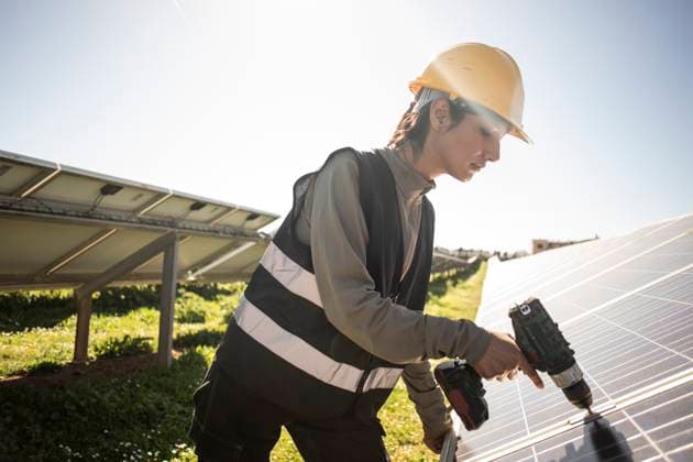 Female engineer using drill while working near solar panels at power station Spain, Mallorca, model released, property released Copyright: xMaskotx , MA107792 MA107792