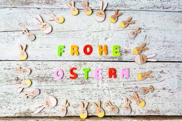 3 March 2024: Happy Easter, lettering made of colorful letters next to cheerful wooden Easter bunnies *** Frohe Ostern, Schriftzug aus bunten Buchstaben neben fröhlichen Osterhasen aus Holz