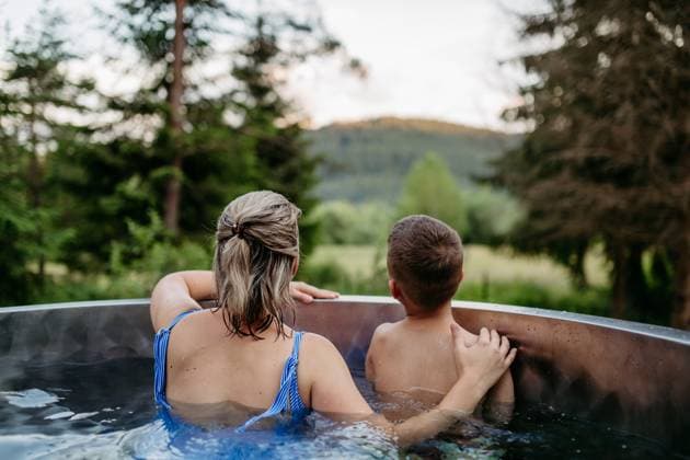 IMAGO Creative, Jahreszeit Sommer, Hitze Mother with her little son enjoying view at nature while bathing in wooden barrel hot tub in the terrace of the cottage. Mother with her little son enjoying view at nature while bathing in wooden barrel hot tub in the terrace of the cottage. Wooden bathtub with a fireplace to burn wood and heat water. model released