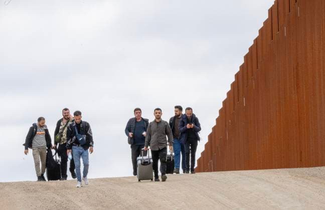 Migrants walk along the United States side of the border wall with Mexico to surrender to the U.S. Border Patrol near Campo, California on March 13, 2024. A bipartisan Senate immigration bill to address the migrant immigration issue is stalled in the House due to election year politics.  CAL2024031403 PATxBENIC