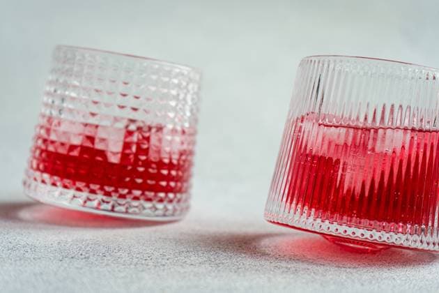 Two textured glasses filled with ice and a vibrant cherry vodka and tonic cocktail, cast on a simple backdrop. Model Released AnnaBogush_ID19984_591799_005 Copyright: xAnnaxBogushx