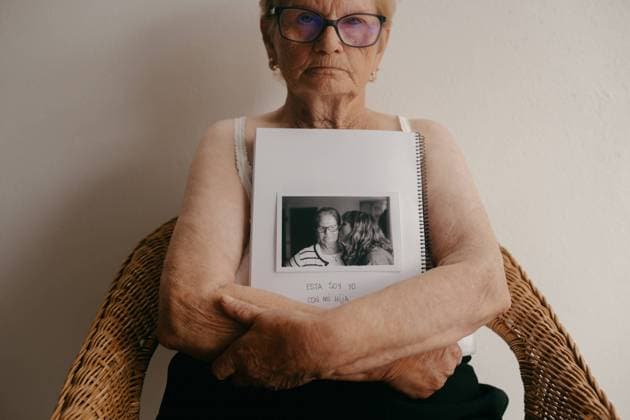 Creative Highlights Symbolbilder MR_ID19651_16395_MariaTeresaViNasFrancisco.jpg, MR_ID19651_16607_JosefinaOvinVinas.jpg An elderly woman with glasses sits holding a photo album open to a page with a black and white picture of herself and a younger family member Model Released EmmaOvin_ID19651_582684_001 Copyright: xEmmaxOvinx RECORD DATE NOT STATED