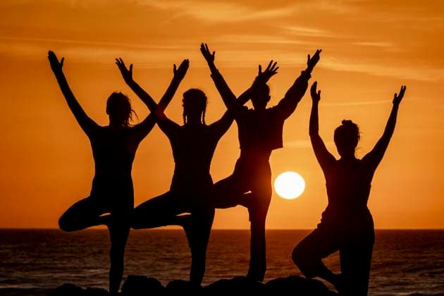 Creative Highlights Symbolbilder A group of women perform various yoga poses in silhouette against a vibrant sunset on the beach, demonstrating harmony with nature. Model Released JuanAizpuru_ID19654_582801_050 Copyright: xJuanxAizpurux