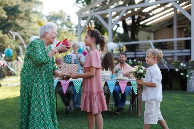 Garden birthday party for senior lady. Beautiful senior birthday woman receiving gift from grandchildren. Garden birthday party for senior lady. Beautiful senior birthday woman receiving gift and flowers from grandchildren. model released