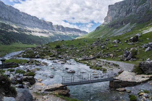 A tranquil river flows through the Ordesa Valley with a simple bridge crossing, set against the majestic backdrop of the Ordesa y Monte Perdido National Park cliffs Model Released JuanLopez_ID19920_590343_007 Copyright: xJuanxLopezx