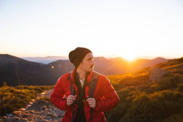 Young man with backpack standing on a mountain trail, gazing into the sunset with a thoughtful expression. Model Released PabloMenendez_ID19716_584647_010 Copyright: xPabloxMenendezx