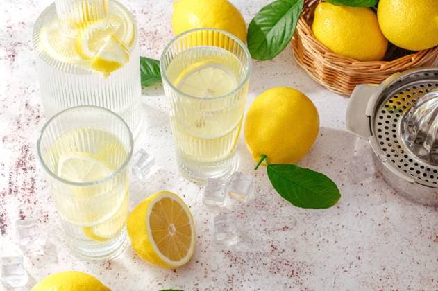 summer lemon lemonade in a glass and decanter. Lemons are scatte CR_KUAL240313-1366534-01