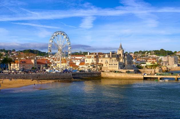 Schöner Blick auf Cascais, Portugals Küstenstadt in der Nähe von Lissabon. Uferpromenade mit Strand und Fischersteg, Wahrzeichen Palacio Seixas und Riesenrad am Ufer an einem sonnigen Tag, klarer blauer Himmel und Wolken, ruhiges Meerwasser *** Beautiful View at Cascais, Portugal Coastal city in the Proximity from Lisbon Waterfront promenade with Beach and Fishing pier, Landmark Palacio Seixas and Ferris wheel on Shore to a sunny Day, Clearer Blue Sky and Clouds, quiet Seawater Copyright: imageBROKER NatalliaxPershaj ibxnpe10331770.jpg