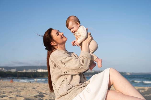 Smiling woman sitting on sand and playing with baby girl at beach model released, Symbolfoto, ALKF00994